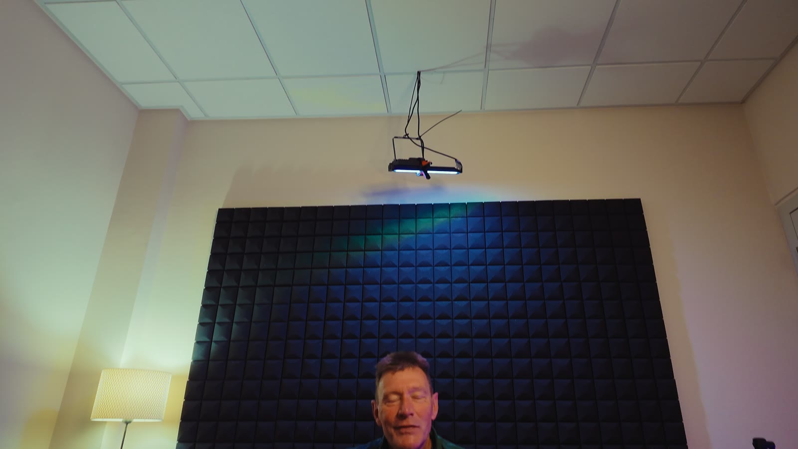 De set van opzij: Cees in zijn stoel, met een microfoonstandaard en een staande lamp