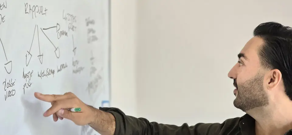 Djahed wijst met een stift naar een rapport dat hij op een whiteboard uittekent