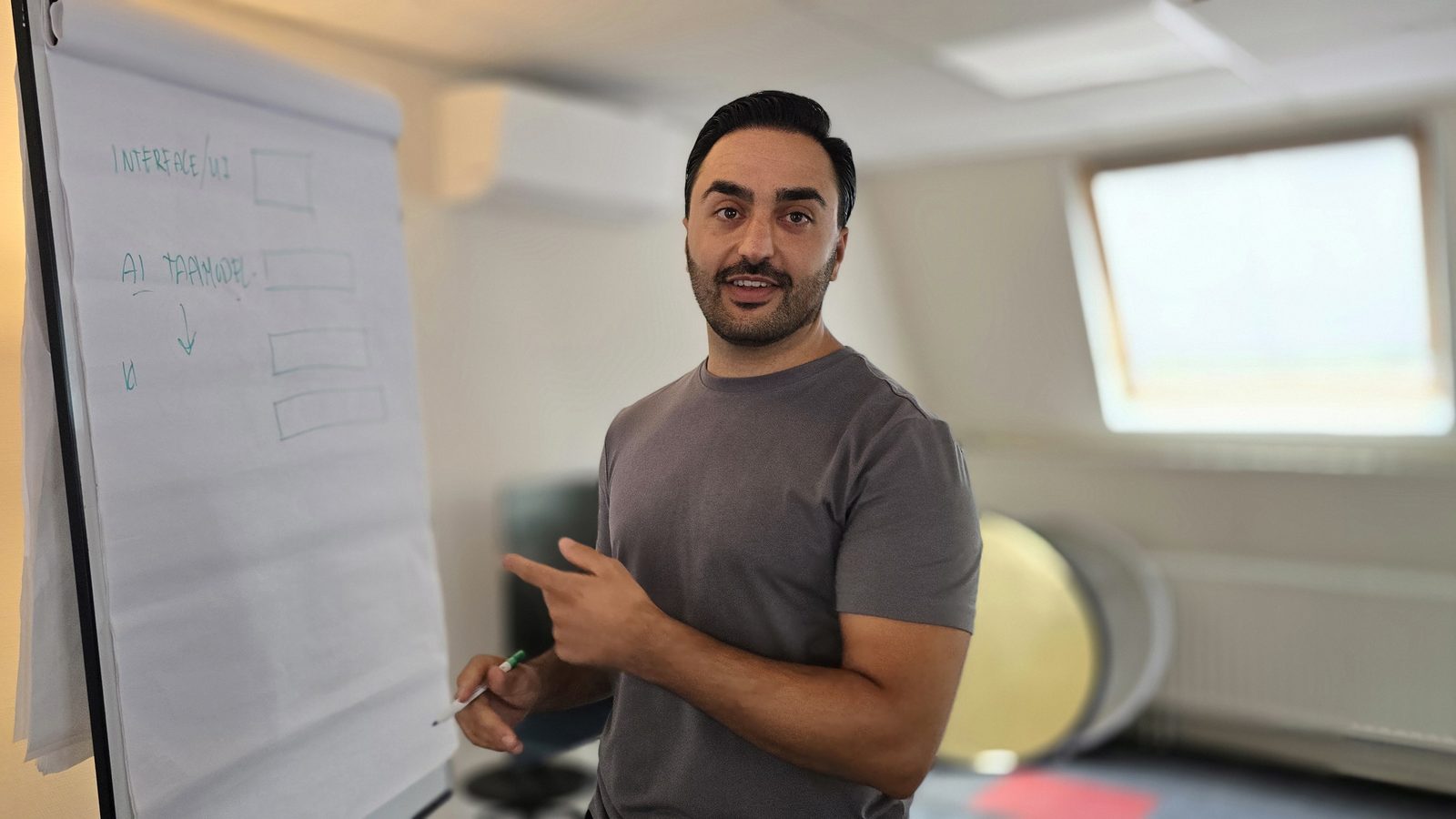 Djahed Atayi legt de lagen uit bij een flipover, met een pen in zijn hand