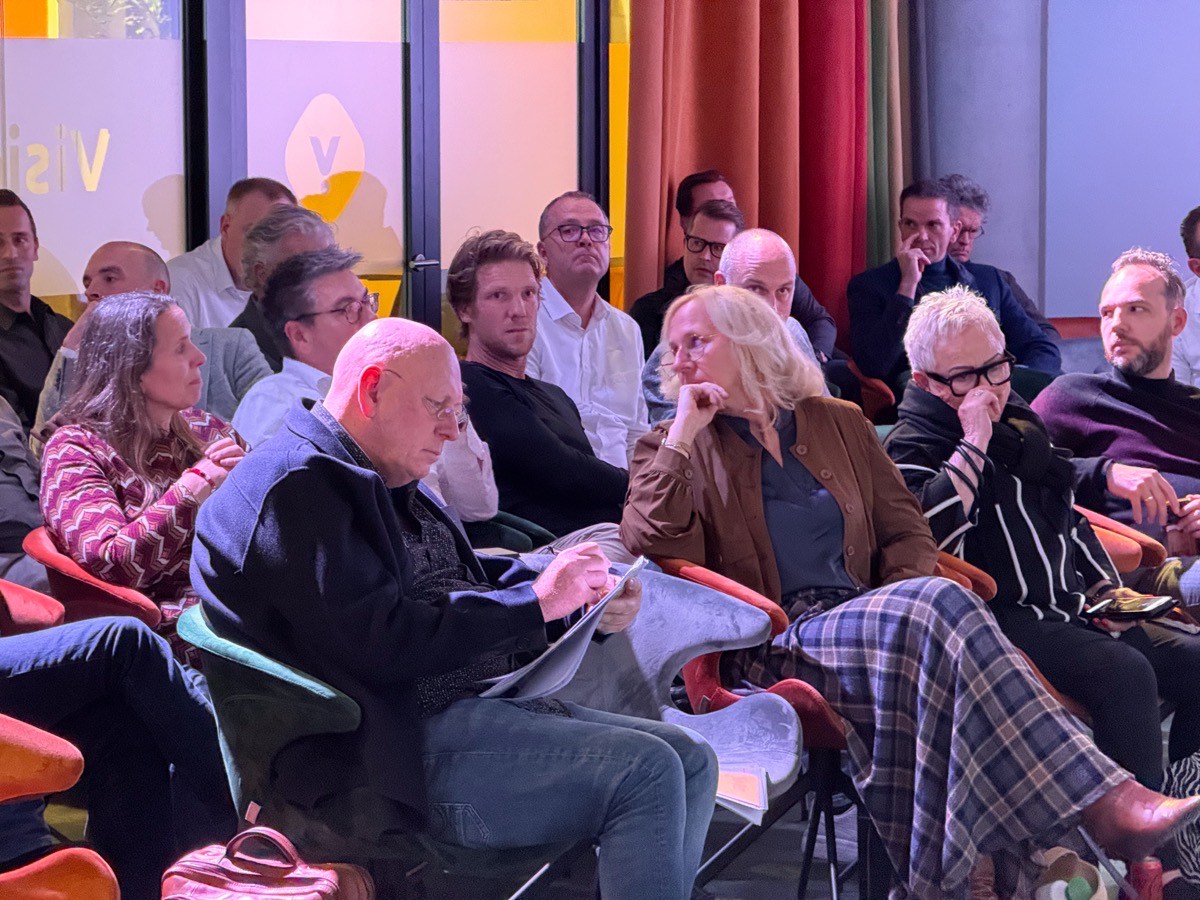 Een zaal vol ondernemers en directeuren die naar een presentatie luisteren; een vrouw steunt haar kin op haar hand, een man leest mee in zijn aantekeningen.