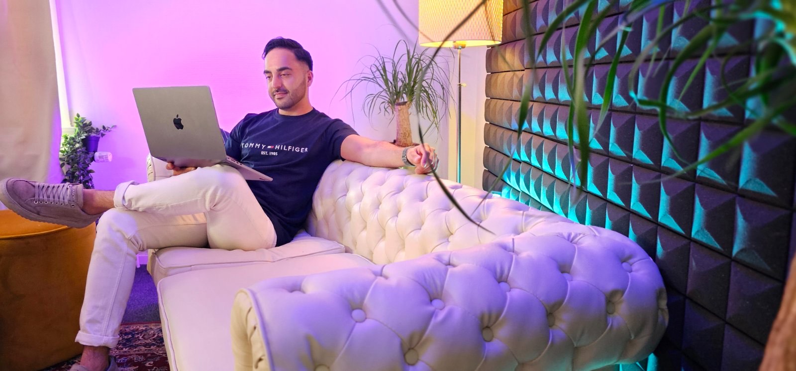 Djahed Atayi met een laptop op een witte chesterfieldbank in de studio