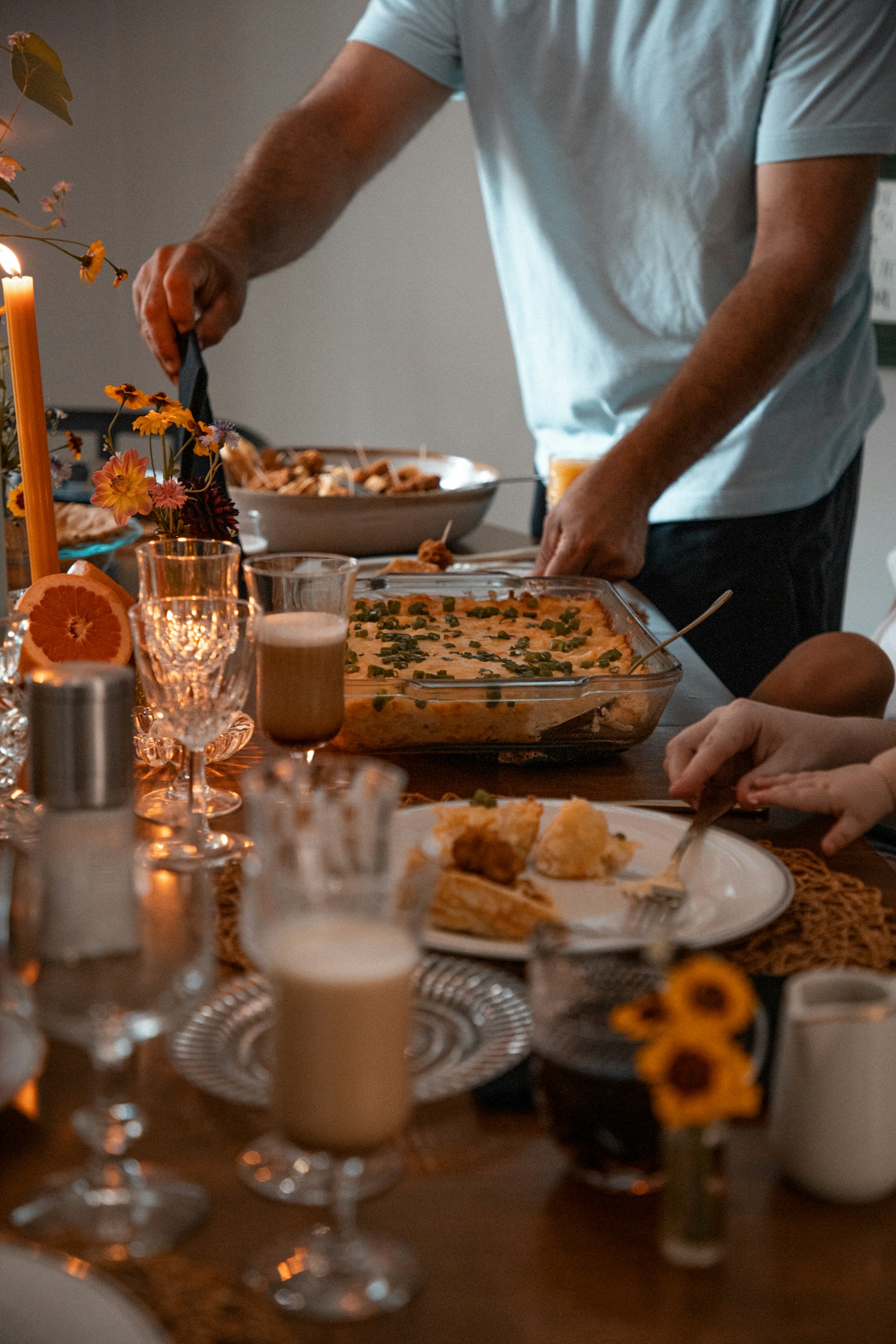 Iemand schept eten op aan een gedekte tafel met kaarsen en bloemen