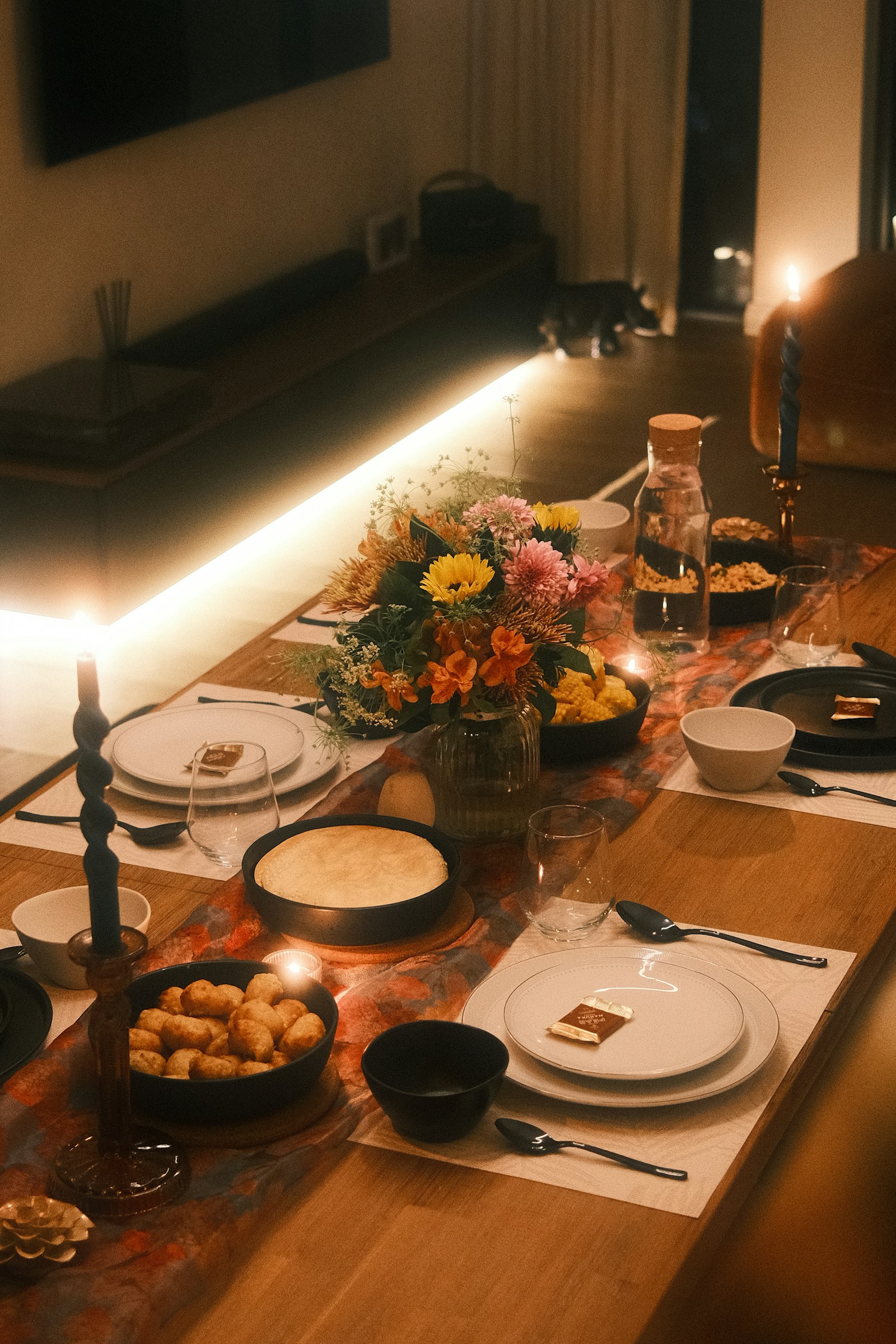 Een lange gedekte tafel met kaarsen en bloemen in een donkere ruimte